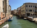 A canal in Venice, Italy on a quiet summer morning. Boats line the side of the canal with a few people walking beside the canal